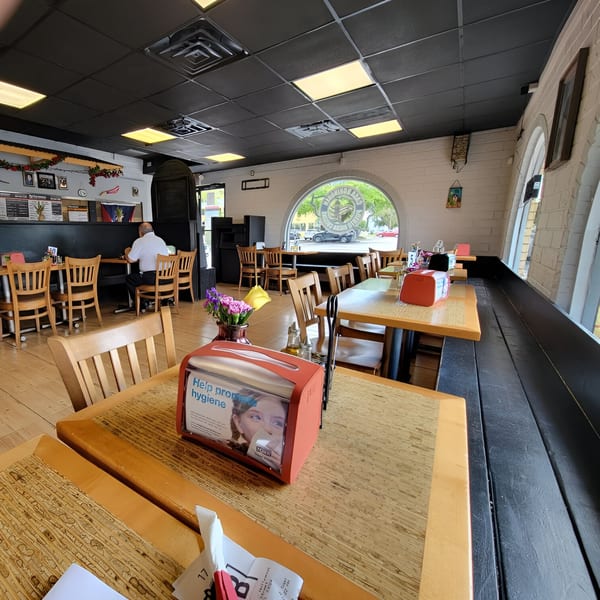 Interior of Casa Borinquen with wooden tables, chairs, and a large arched window overlooking the street.