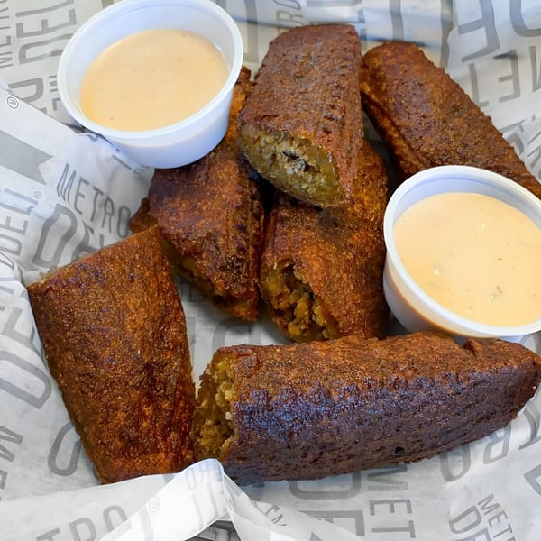 A basket of golden-brown alcapurrias, a Puerto Rican fritter, with two cups of dipping sauce.