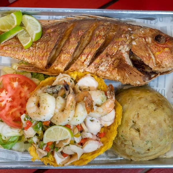 A whole fried snapper with lime, shrimp and seafood salad in a plantain basket, and mofongo.