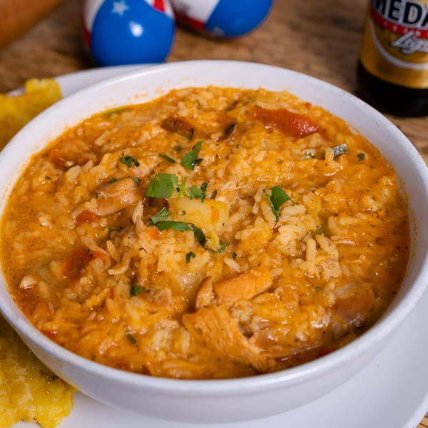 Close-up of a bowl of Arroz con Pollo, a Puerto Rican chicken and rice dish, with plantains and beer.