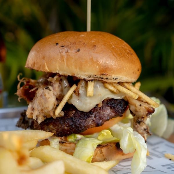 Close-up of a Casa Borinquen burger with melted cheese, shredded pork, and shoestring fries.