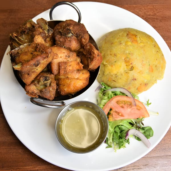 Fried chicken pieces in a metal bowl, with mofongo, a side salad, and dipping sauce.