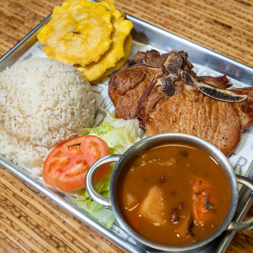 Casa Borinquen's Puerto Rican meal with pork chops, rice, plantains, salad, and a side of soup.