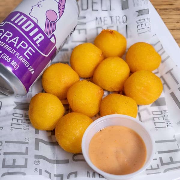 Golden-fried alcapurrias, a Puerto Rican fritter, with dipping sauce and a can of India Grape soda.