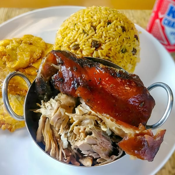 Puerto Rican dish with roasted pork, yellow rice with beans, and fried plantains on a white plate.