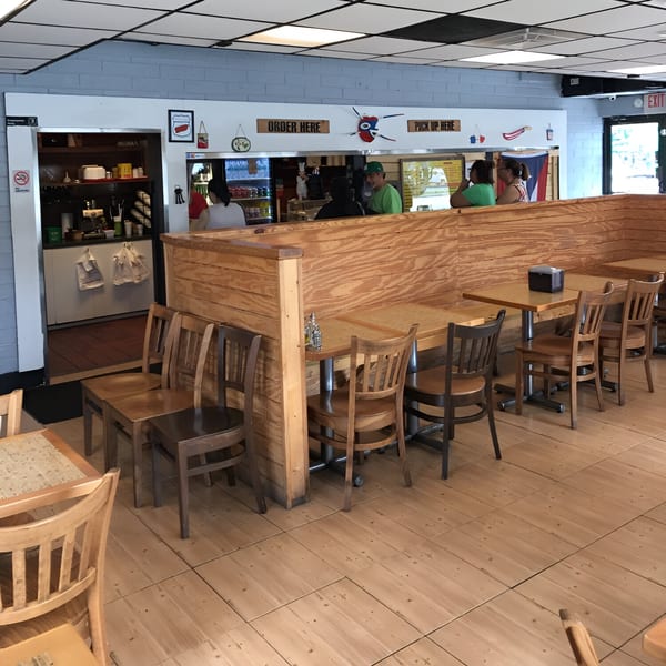 Interior of Casa Borinquen with wooden booths, tables, chairs, and customers at the counter.